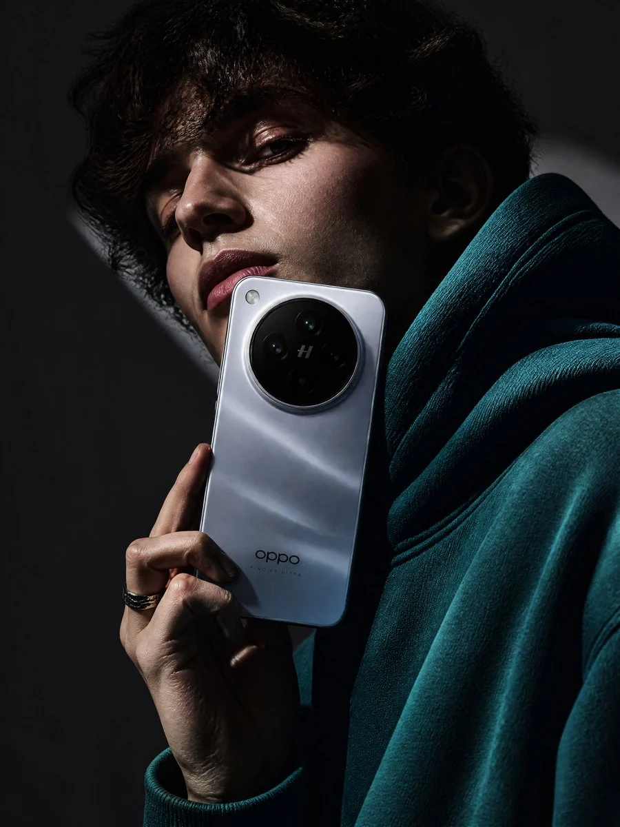 A stylish young woman in a teal hoodie holding an OPPO Find X9 Ultra smartphone to her eye, showcasing its camera system against a deep teal background, embodying a luxury tech advertisement.